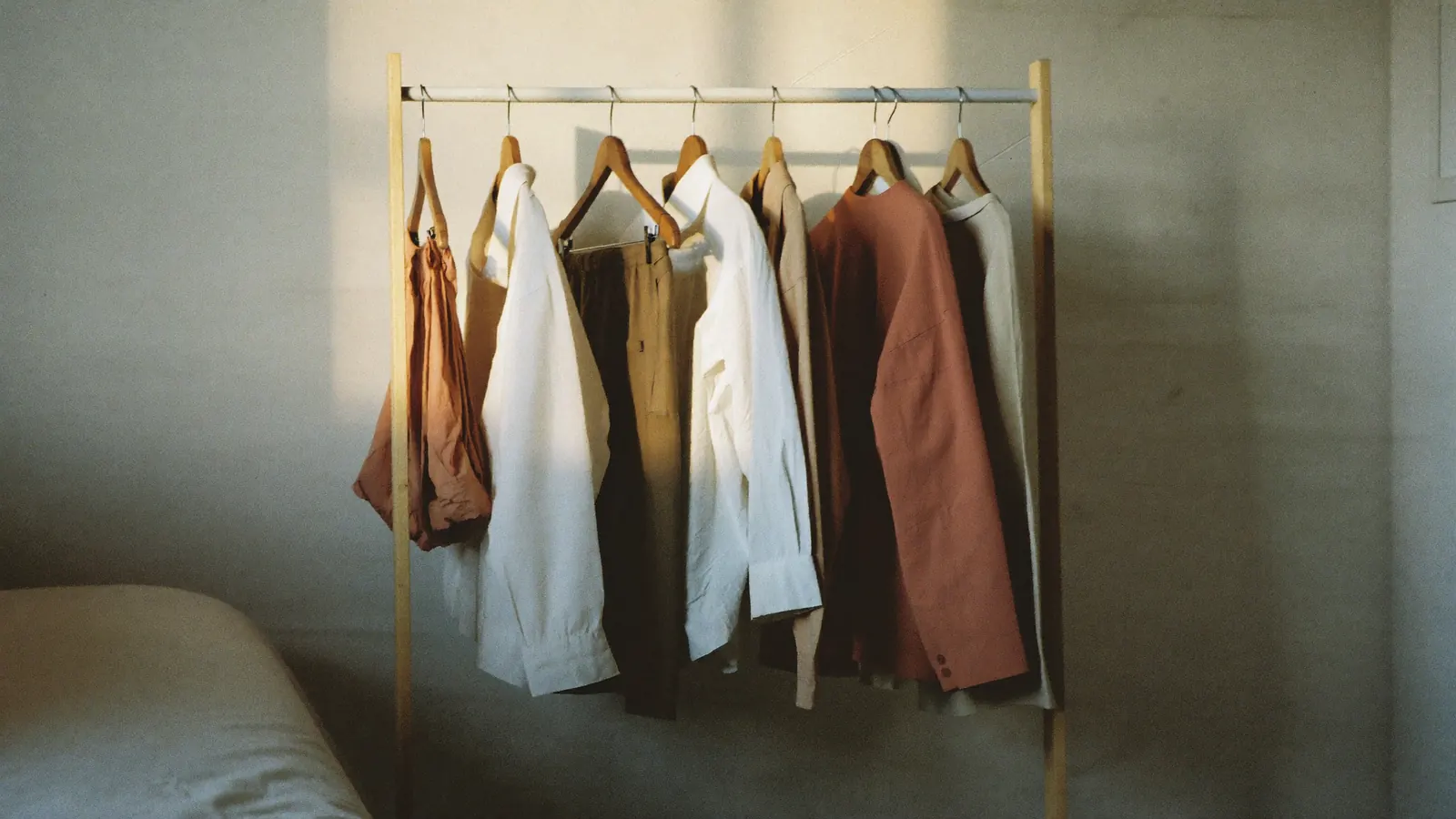 Illustration: a simple clothing rail holding everyday garments in warm neutrals, in morning light.